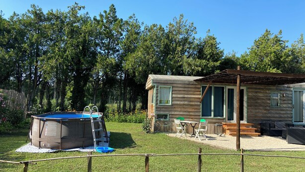 Una baita di legno con patio, un trampolino e un cortile recintato.