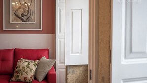 A red sofa with floral cushions, a framed artwork above it, and a white door with a textured wall behind.