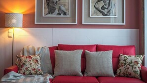 A red sofa with floral and checkered cushions, a floor lamp, and framed artwork on the wall.