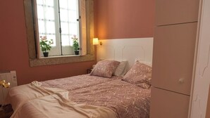 A bedroom with two beds, a window with a view of flowers, a bedside lamp, and a wardrobe.
