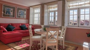 A living room with a red sofa, white chairs, a round table, and large windows with white frames. - Porto Clérigos Apartment Violet (4th) (Porto)