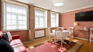 A room with a red sofa, a dining table with white chairs, a TV mounted on the wall, and large windows with white frames. - Porto Clérigos Apartment Violet (4th) (Porto)
