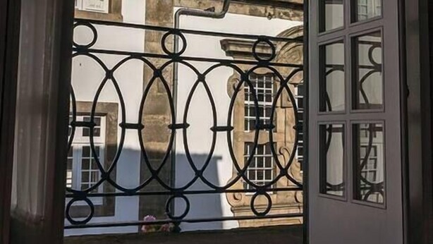 A window with a wrought iron balcony overlooking a building with a statue and a tiled roof. - Porto Clérigos Apartment Violet (4th) (Porto)