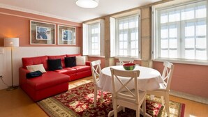 A red sofa, white chairs, a dining table, and a large window with white shutters.
