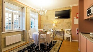 A dining area with a round table, white chairs, a chandelier, and a stone wall.