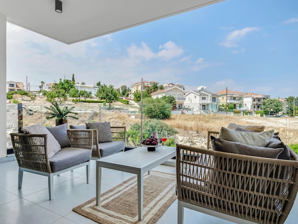 A modern outdoor seating area with wicker furniture and a glass table, overlooking a residential neighborhood with houses and greenery.