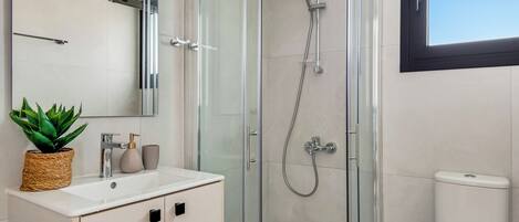 A modern bathroom with a glass-enclosed shower, a white sink, a mirror, and a potted plant.