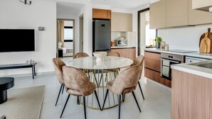 Cozinha moderna com ilha central, eletrodomésticos embutidos e área de jantar com mesa redonda e cadeiras.