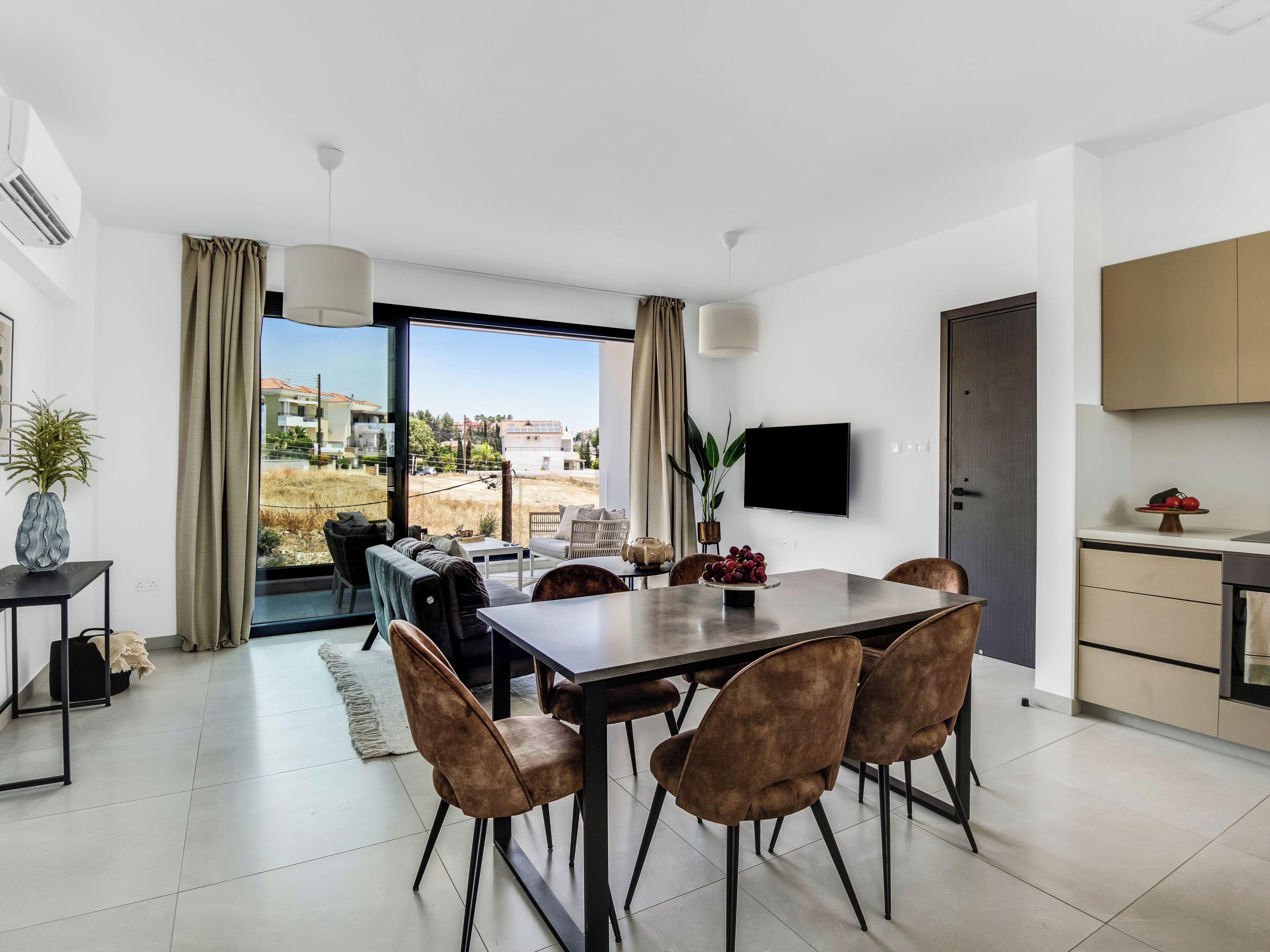 Un espace repas moderne avec une grande table et des chaises, un téléviseur à écran plat fixé au mur et une vue sur l’extérieur.