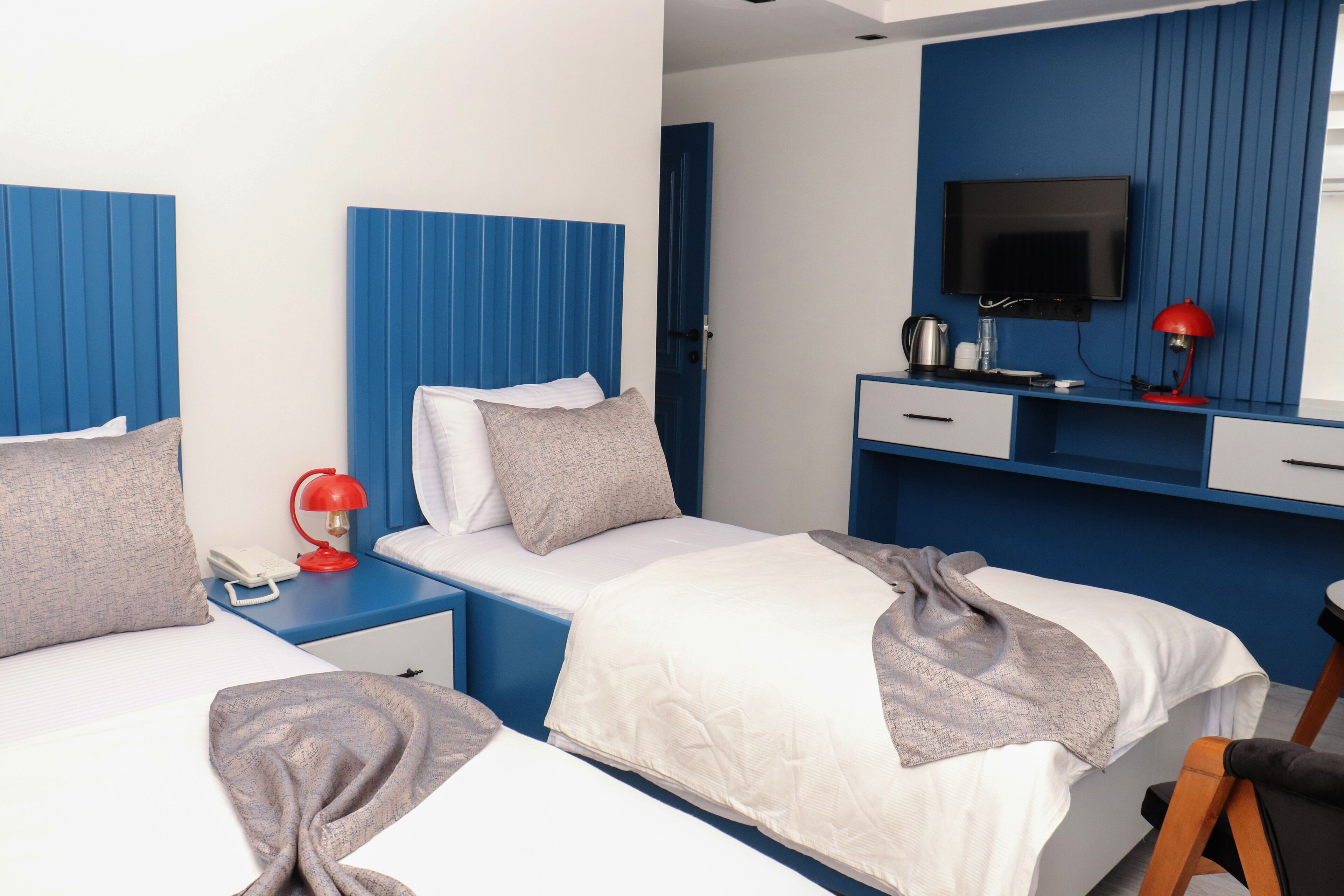 A hotel room with two beds, a TV, a desk with a computer, and a red lamp.