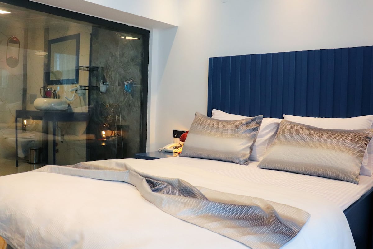 A modern hotel room with a large bed, a glass shower enclosure, and a blue headboard.