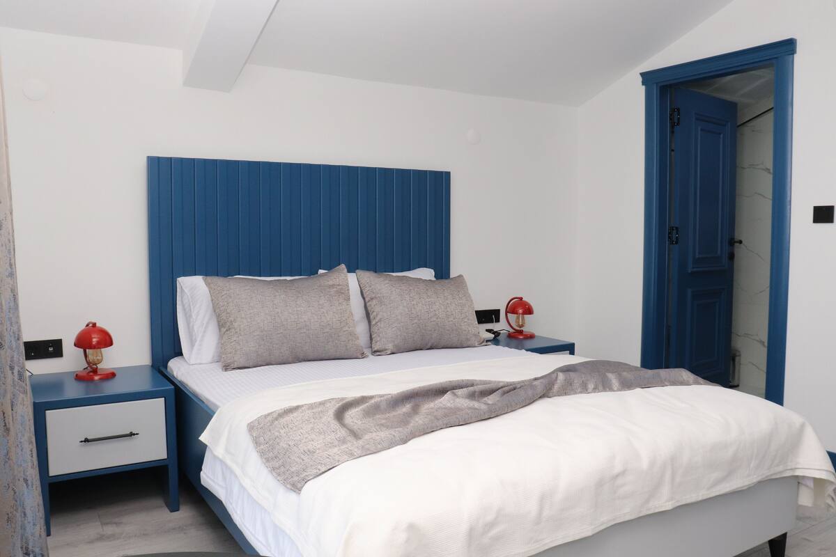 A bedroom with a blue headboard, white bedding, and a red lamp on the nightstand.