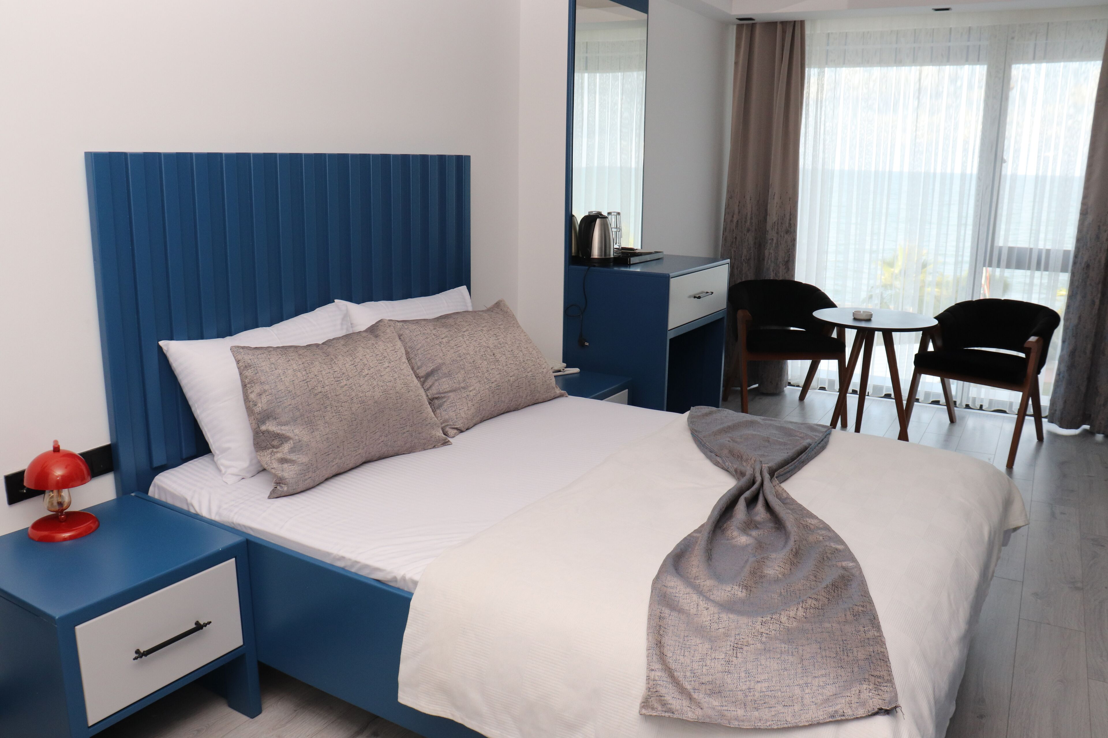 Una habitación de hotel con cama, escritorio, silla y ventana con cortinas.