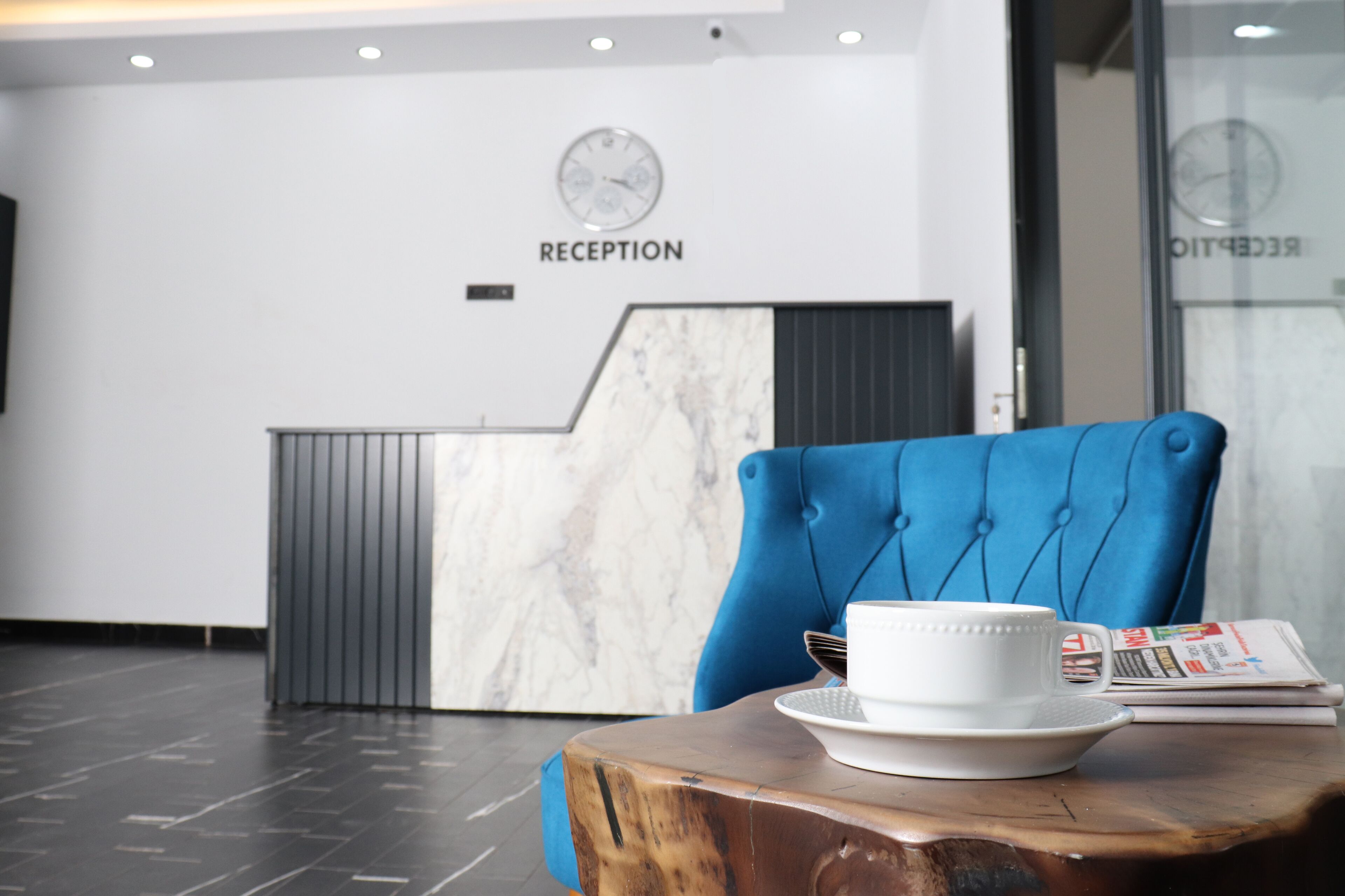 Un espace d’accueil avec un mur en marbre, une horloge et un fauteuil bleu.
