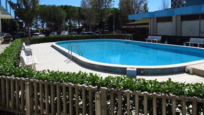 A swimming pool with a wooden fence, benches, and a paved walkway. - Beautiful Sea Front Apartment With Swimming Pool by Beahost Rentals (Caorle)