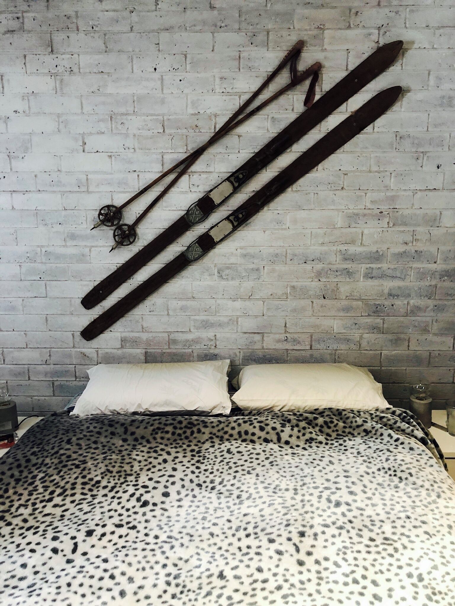 A bed with a leopard print bedspread and two white pillows against a brick wall.