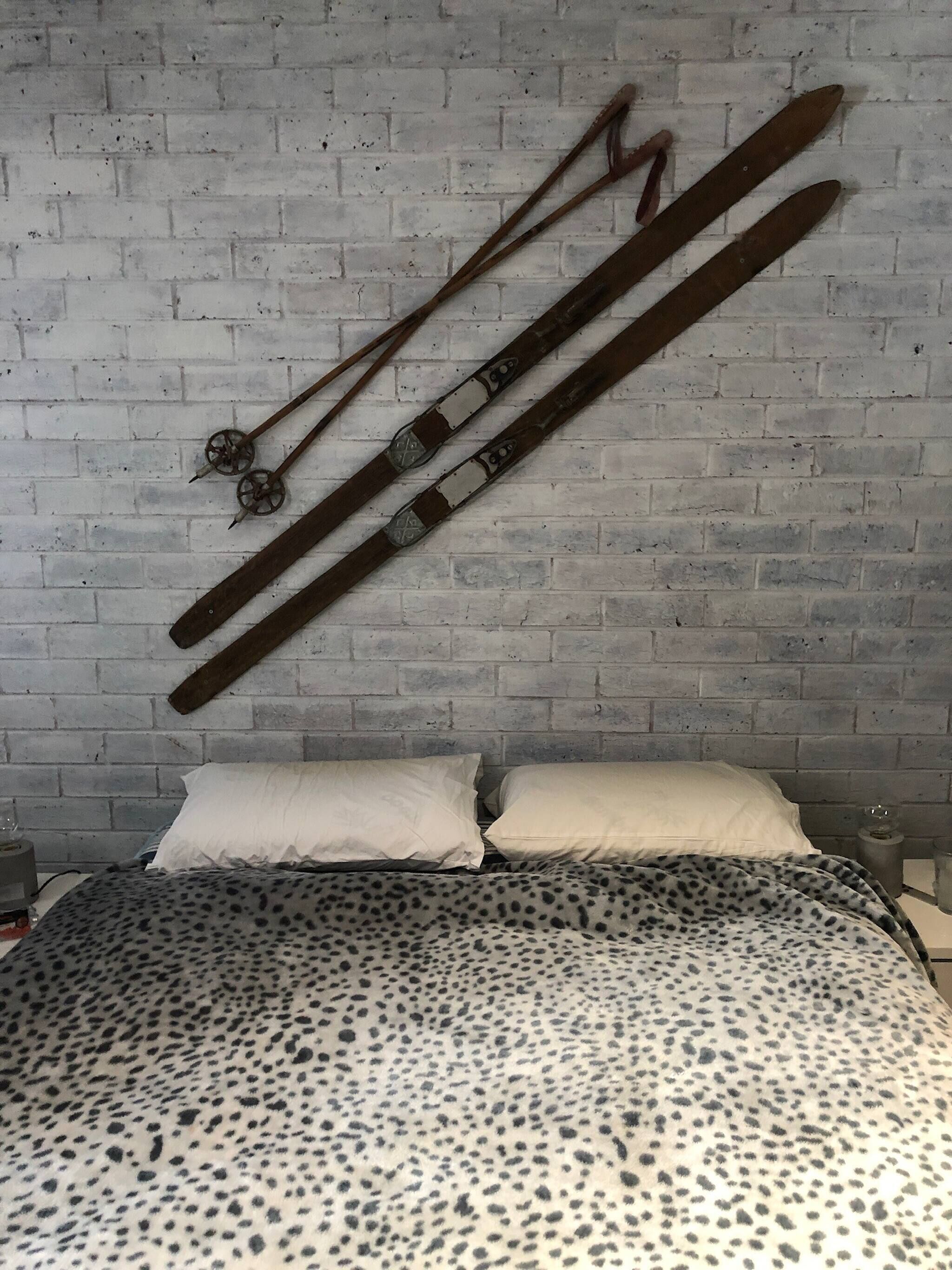Una cama con colcha de estampado de leopardo, una pared de ladrillo blanco y dos esquíes apoyados en la pared.