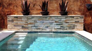 Una piscina con un muro de piedra y tres macetas.
