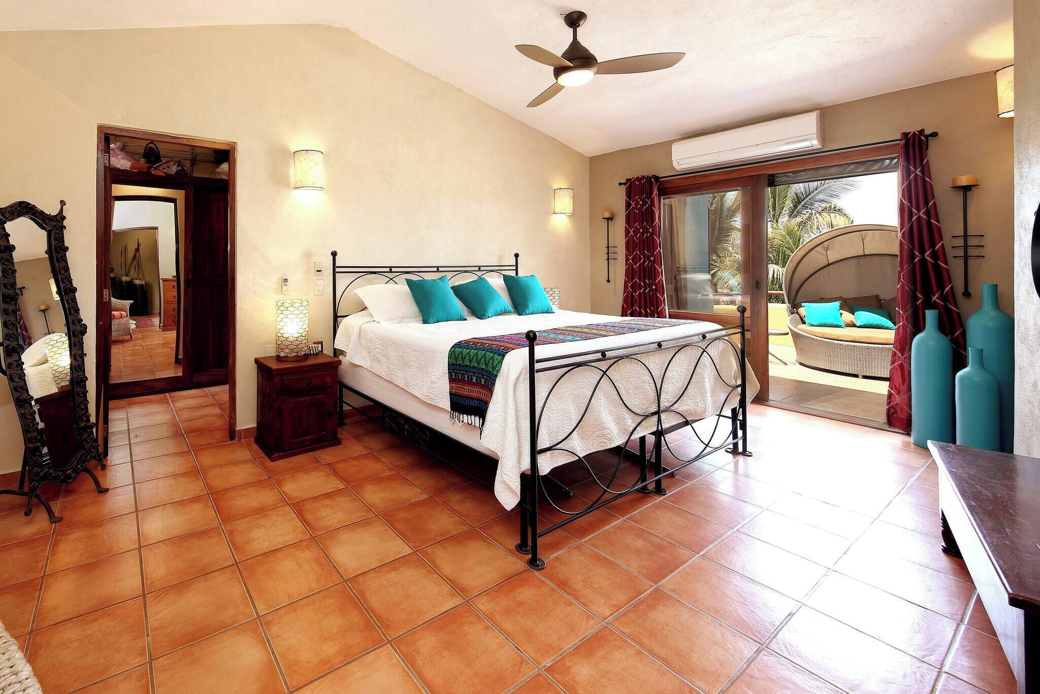 A bedroom with a bed, a ceiling fan, a nightstand, a mirror, and a view of the outside.