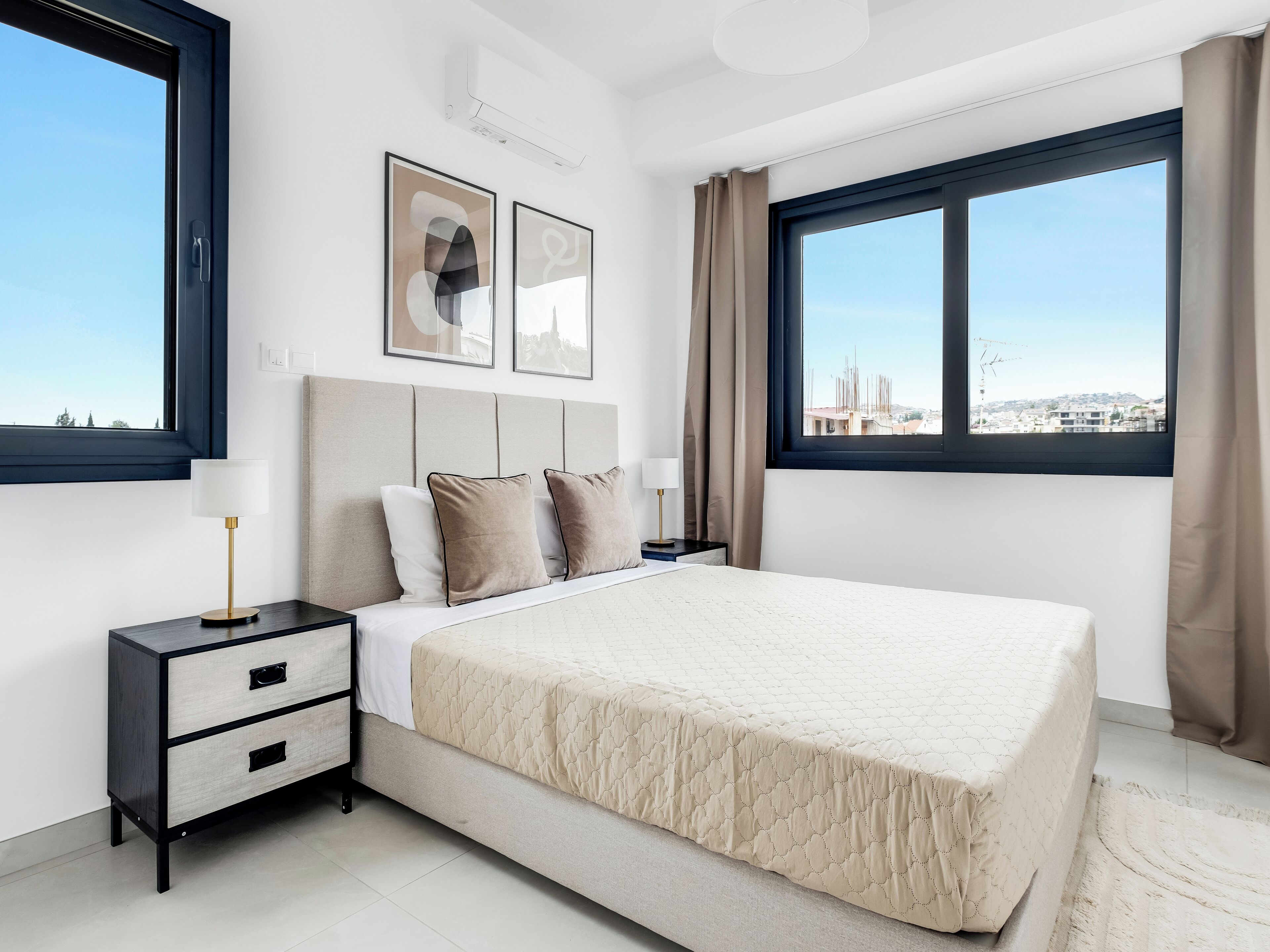 A modern bedroom with a large bed, a bedside table with a lamp, and two framed pictures on the wall.