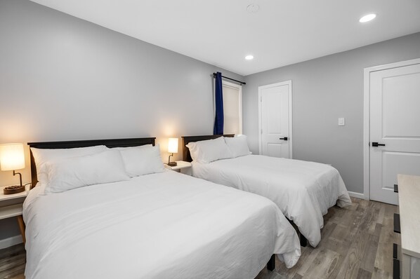 A hotel room with two single beds, a nightstand with a lamp, a door, and a window with curtains.