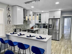 A modern kitchen with white cabinets, a stainless steel refrigerator, a central island with bar stools, and pendant lighting.