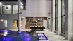 A modern indoor pool area with a seating area and a kitchen in the background. - Grandhalla - the Pinnacle of Luxury in Orlando (Kissimmee)