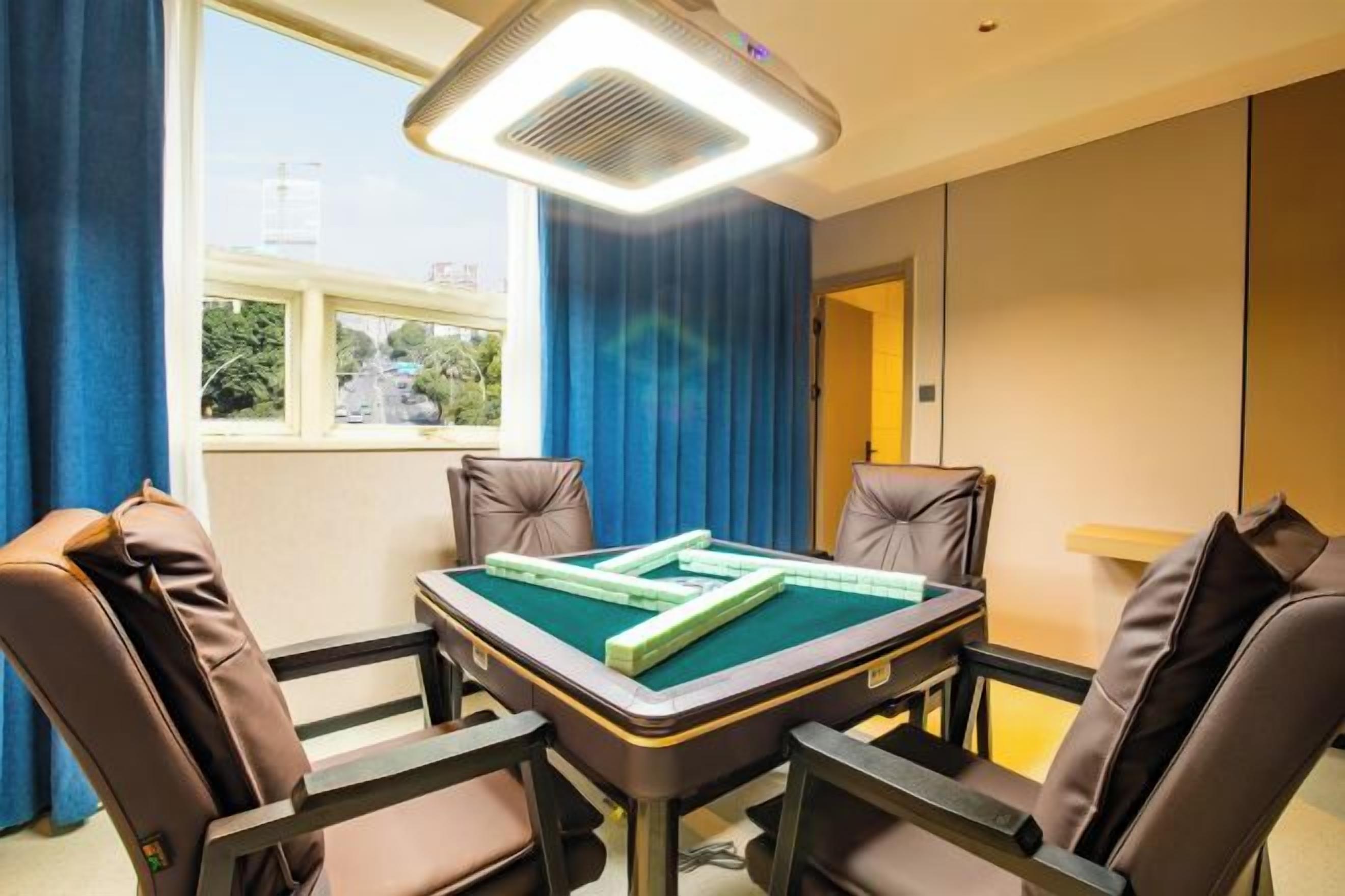 A room with a pool table, four leather chairs, a ceiling fan, and a window with a view of buildings and trees.