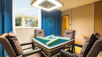 A room with a pool table, four leather chairs, a ceiling fan, and a window with a view of buildings and trees.