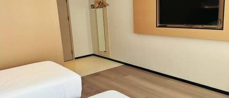 A hotel room with two beds, a flat-screen TV mounted on the wall, and a wooden floor.