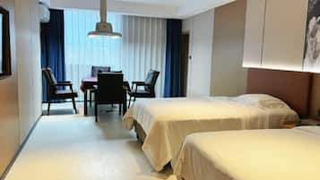 A hotel room with two beds, a desk with chairs, and a large window with curtains.