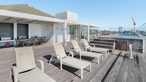 Eine Dachterrasse mit Korbsesseln, einem Pool und einem Essbereich mit Gartenmöbeln.