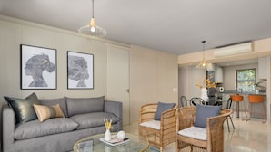 Ein modernes Wohnzimmer mit einem grauen Sofa, Korbstühlen, einem Glastisch und Kunstwerken an der Wand.