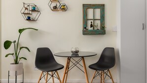 Un comedor con una mesa redonda, dos sillas negras, una planta en maceta y estantes hexagonales en la pared con objetos decorativos.