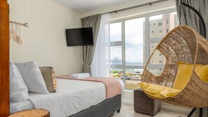 Un dormitorio con cama, televisión, una silla de mimbre y vistas a la ciudad.