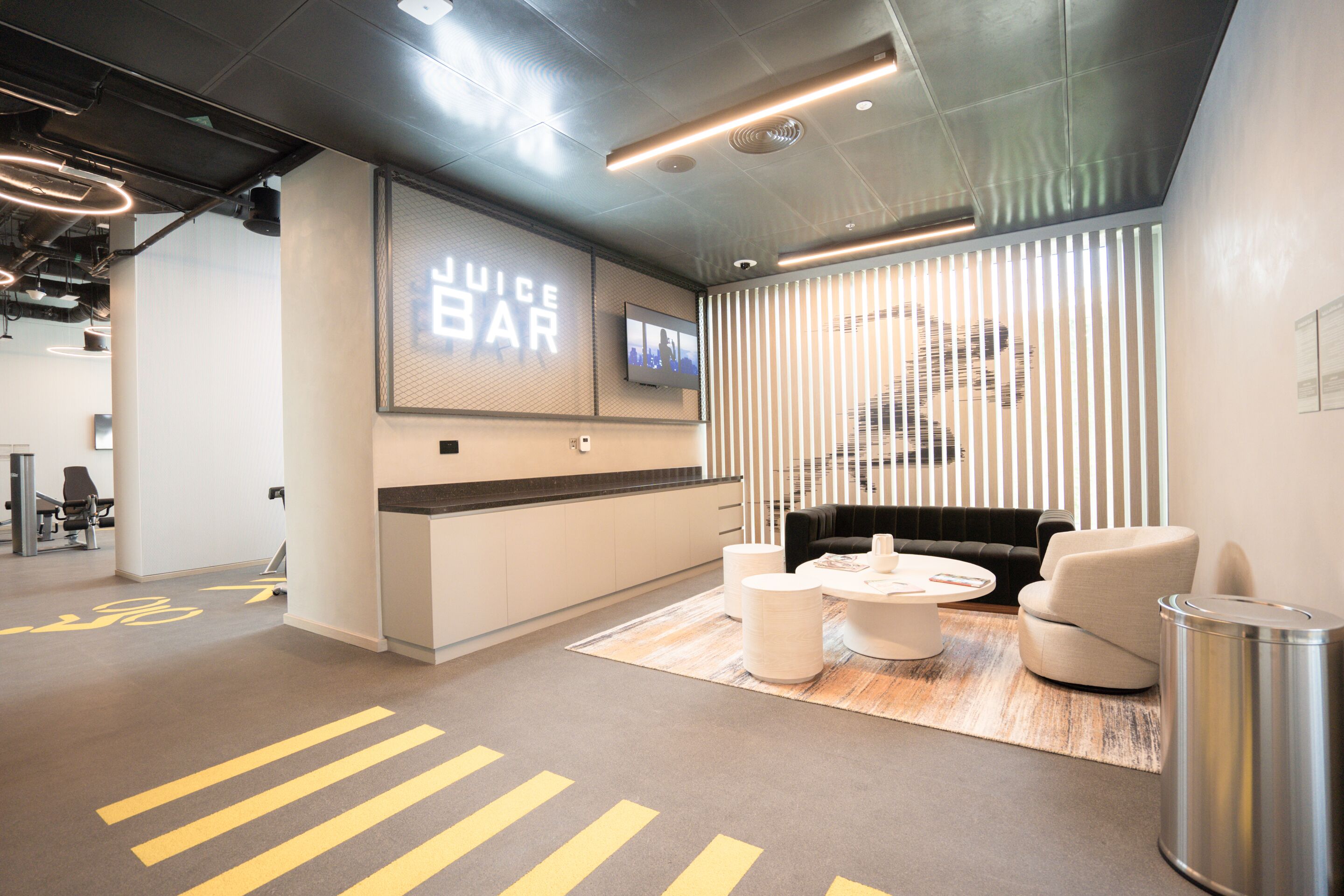 Un espace de bureau moderne comprenant un espace d’accueil, des sièges et un grand écran affichant le texte « Bar à jus ».