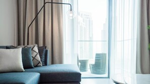 Een moderne woonkamer met een bank, kussens, een vloerlamp en uitzicht op hoge gebouwen door grote ramen.