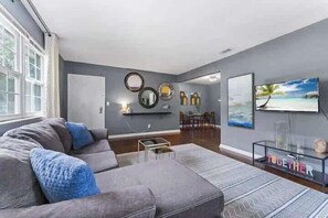 A modern living room with a grey sofa, a coffee table, a TV, and wall art.