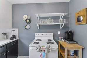 A kitchen with a stove, white shelves, and a coffee maker. - Eclectic Escape #4 | Team Joseph Ellen (Jacksonville)