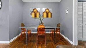 A dining area with a glass table, four chairs, and a vase with flowers. - Eclectic Escape #4 - Team Joseph Ellen (Jacksonville)