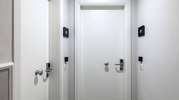 Una puerta blanca con cerradura electrónica por teclado y timbre. En la pared, dos letreros negros con los números "101" y "102".