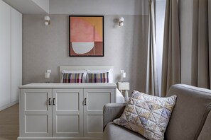 A modern bedroom with a white bed, a beige sofa, and a large abstract painting on the wall. - Numa Florence Fiore (Florence)