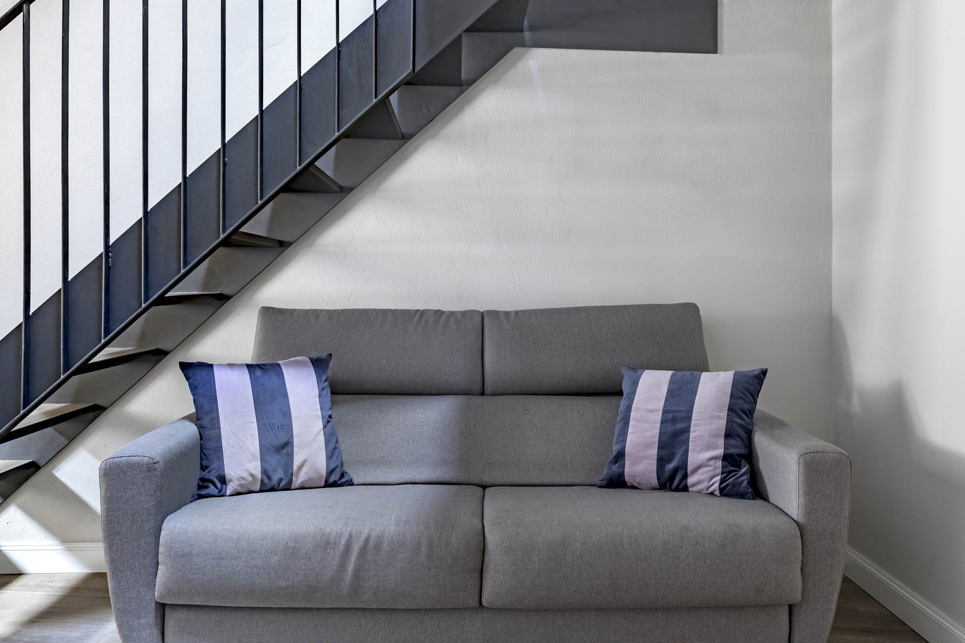 Ein graues Sofa mit zwei gestreiften Kissen in einem modernen Wohnzimmer mit einer Treppe.