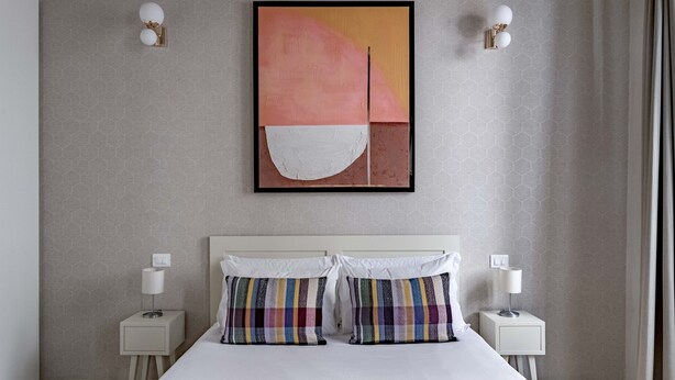 A modern hotel room with a large bed, two bedside tables with lamps, a large abstract painting on the wall, and a patterned wallpaper. - Numa Florence Fiore (Florence)