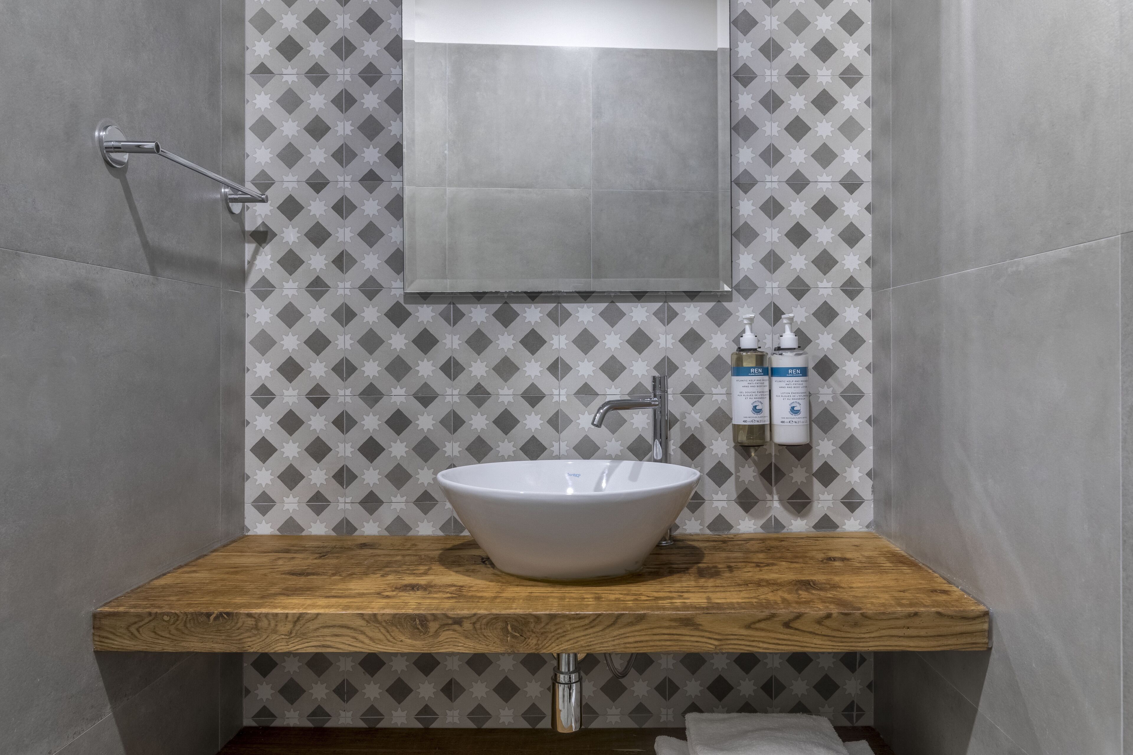 Un baño moderno con tocador de madera, un lavabo blanco tipo tazón y un espejo arriba.