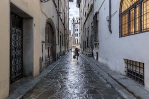 A narrow cobblestone street flanked by buildings with arched doorways and windows with metal grilles. - Numa Florence Fiore (Florence)