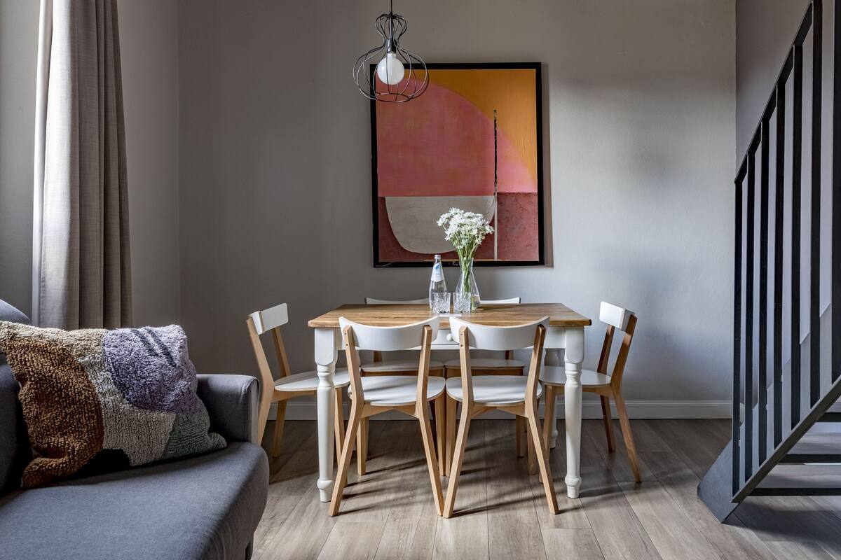 A dining area with a wooden table and chairs, a vase with flowers, and a painting on the wall.