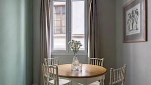 A dining area with a round wooden table, white chairs, a vase with flowers, and a framed botanical illustration on the wall. - Numa Florence Fiore (Florence)