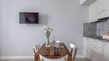 Uma cozinha moderna com uma mesa de jantar de madeira, cadeiras brancas, uma TV montada na parede e um revestimento de parede estampado.
