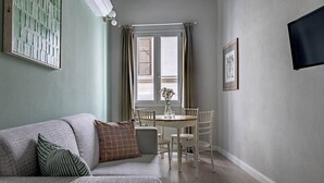 A living room with a sofa, a dining table, and chairs. There is a window with curtains, a framed picture on the wall, and a flat-screen TV mounted on the wall. - Numa Florence Fiore (Florence)